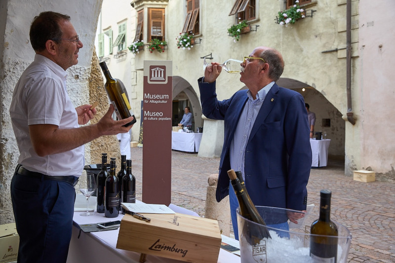 A photo of a man describing the wine to a man tasting it