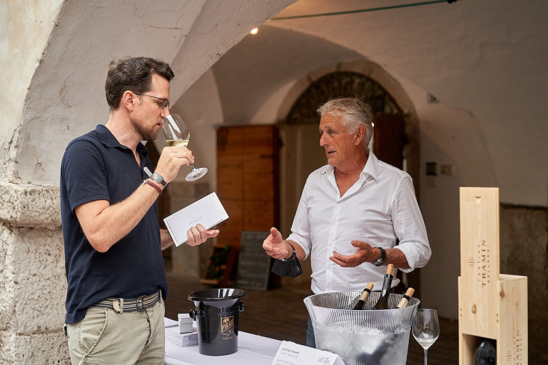 A photo of a man describing the wine to a man who is tasting it